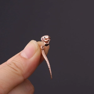 Macro shot of rose gold snake-shaped cartilage stud earring held between fingers