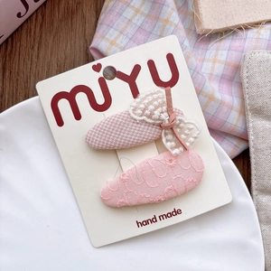 Close-up of pink fabric hair clips with lace bow and embroidery on a display card