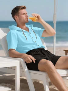 Linen set featuring a sky blue hooded shirt and black shorts in a beach resort setting