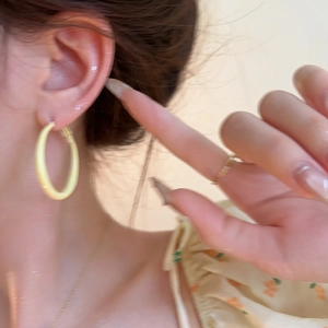 Close-up of minimalist pale yellow hoop earring worn by a model for a summer look