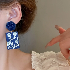 Close-up of blue rose earrings with floral pendants worn by a model for a vintage look