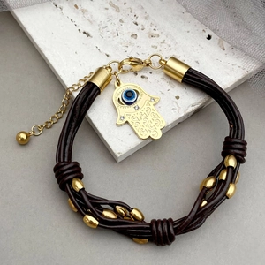 Close-up of leather woven bracelet featuring a gold Hamsa Hand and blue Evil Eye charm