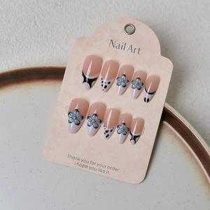 Détail de faux ongles amande avec fleurs bleues et pointes françaises noires élégantes