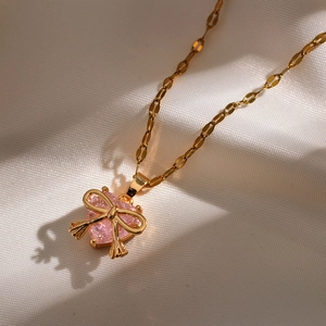 Gold necklace featuring a pink heart pendant and bow detail on white silk background