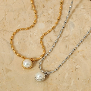 Elegant gold and silver stainless steel necklaces with round pearl pendants on marble