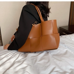 Detailed view of brown woven PU leather tote bag worn on shoulder by a model
