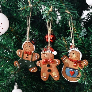 Three festive Christmas gingerbread man resin ornaments hanging on a green Xmas tree branch