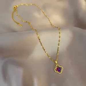 Detail of gold four-leaf clover necklace with iridescent purple gem and white crystals
