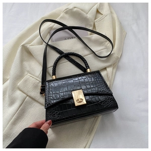 Detail of black crocodile texture handbag with gold metal clasp and woven handle