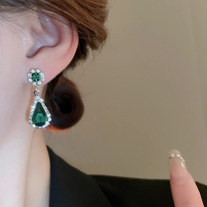 Close-up of model wearing luxury green teardrop earrings with a diamond halo design