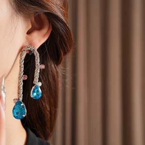Close-up of vintage silver twisted earrings with blue teardrop stones worn by a model
