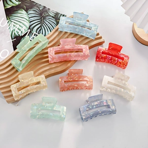 Colorful acetate claw clips with marble texture on a wooden tray for summer hair styling