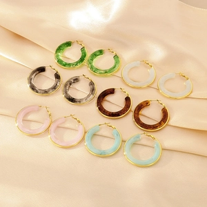 Macro detail of colorful resin C-hoop earrings with golden metal edges on silk