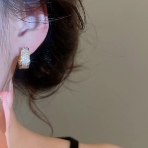 Close-up of sparkling zircon gold huggie earrings worn on model's ear with warm lighting