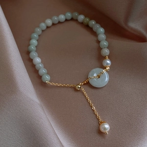 Detail of light green jade beads and white pearls bracelet on a champagne silk fabric