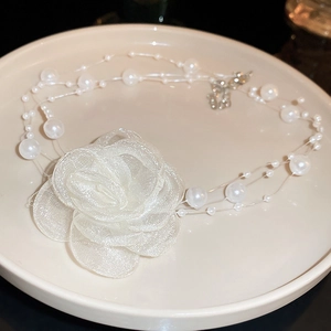 Three-layer faux pearl choker necklace with white mesh flower on a black background