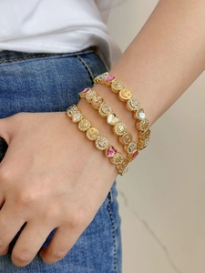 Close-up of gold charm bracelet with pink heart rhinestones and yellow smiley face charms