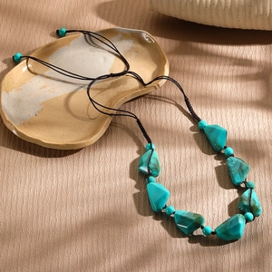 Macro shot of turquoise and pearl beaded necklace on a textured ceramic tray