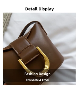 Close-up of brown leather bag featuring a polished gold horseshoe-shaped buckle detail