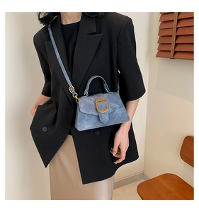 Close-up of blue suede crossbody bag with gold woven buckle on a model in blazer