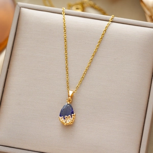 Elegant gold necklace with a teardrop blue gemstone pendant on a gray jewelry box