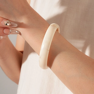 Close-up of a minimalist cream white resin wide bangle on model wrist with soft lighting