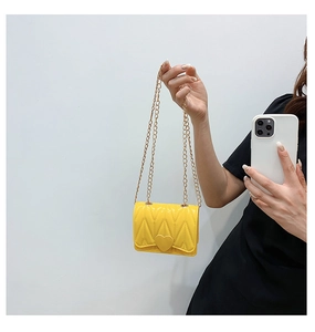 Detail of yellow quilted silicone heart crossbody bag with gold metal chain strap
