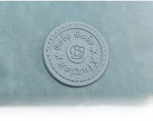 Close-up of the BoBo brand logo patch and stitching detail on the light blue crossbody bag