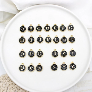 Detailed view of 26 black and gold alloy alphabet charms arranged on a white ceramic plate