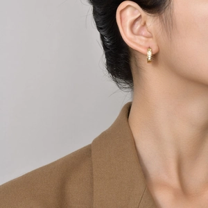 Close-up of gold stainless steel hoop earrings with white zircons on a model's ear