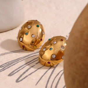 Macro shot of 18K gold plated oval earrings with colorful zircon stones on ivory fabric