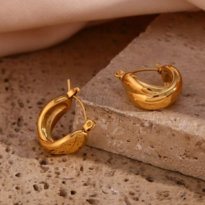 Close-up of golden chunky twisted hoop earrings on stone surface with pink silk background