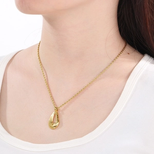 Close-up of a gold twisted teardrop pendant on a refined rope chain worn by a model