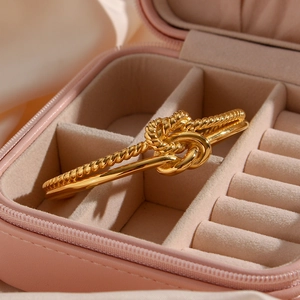 Close-up of golden twist knot bangle with dual-strand design in a pink jewelry box