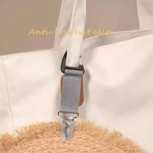 Portable hat clip for travel with grey strap and metal buckle attached to a canvas bag