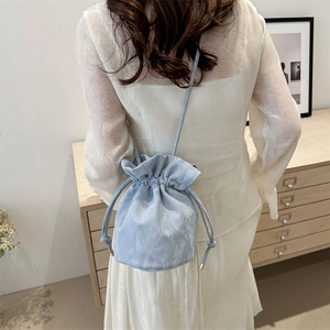 Minimalist light blue drawstring bucket bag with pleated texture on a female model