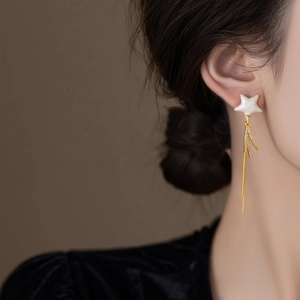 Close-up of elegant gold tassel earrings with sparkling star stud worn by a model