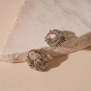 Detail of silver twisted weave texture hoop earrings on white marble stone