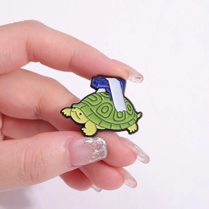 Creative green turtle enamel pin with gun design held by hand against a white backdrop
