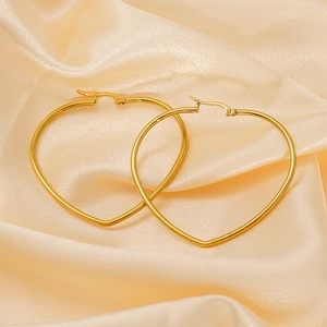 Boucles d'oreilles cœur en acier titane doré poli sur un fond de soie douce couleur champagne