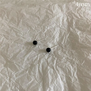 Macro detail of 4mm black onyx stud earring with silver pin on a white paper background