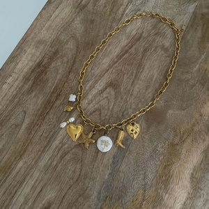 Close-up of a gold charm necklace with heart and palm tree pendants on a wooden surface