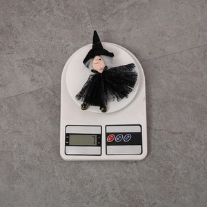 Halloween witch ornament with black sequin skirt and bell being weighed on a digital scale