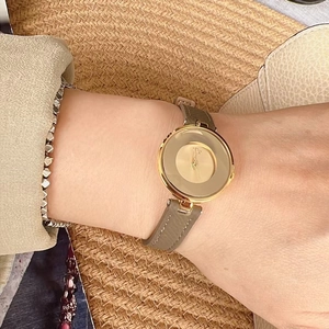 Gold minimalist watch with green leather strap on wrist next to a stylish straw hat
