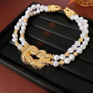 Double-layered baroque pearl necklace with a bold gold-tone knot centerpiece on display