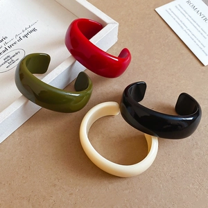 Détail de bracelets joncs en acrylique rouge vert noir et beige sur un plateau