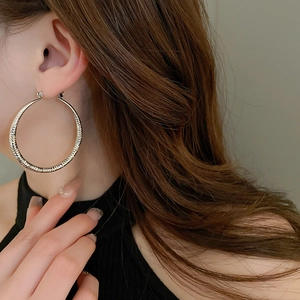 Detail of large silver textured metal hoop earrings shown on model with striped pattern