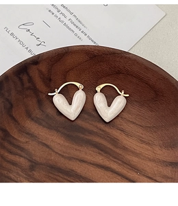 Detail shot of heart-shaped white enamel earrings on a rustic dark wood jewelry tray