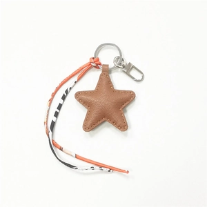 Detail of brown star leather bag charm with silver keychain and patterned silk ribbon