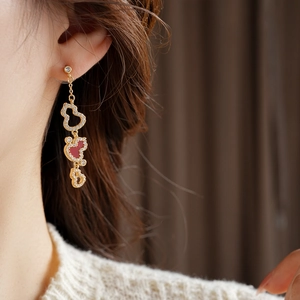 Detailed view of long gold tassel earrings featuring red enamel gourds and white zircons